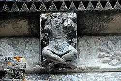 Échebrune – St-Pierre, Kragstein unter Gesims, Person im Schneidersitz