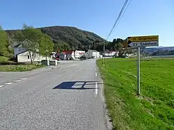 Foto einer Straße die an einigen Häusern vorbeiführt. Im Hintergrund eine Erhebung