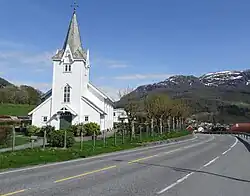 Foto einer Straße und einer weiß gestrichenen Holzkirche in bergiger Landschaft