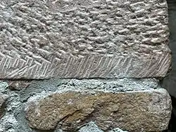 Der obere Stein weist deutliche Bearbeitungsspuren, d. h. eine Faktur, auf. Der untere Stein ist unbearbeitet und zeigt eine körnige, unregelmäßige Textur.