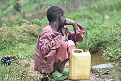 Ein Kind sitzt an einer Wasserstelle in der Hocke. Ein Wasserkanister steht vor ihm.