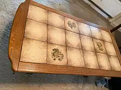 Couchtisch mit 3×6 hellbraunen quadratischen Fliesen und einem breiten dunkelbraunen Holzrand auf einem hellbraunen Teppichboden