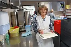 Frau mit weißer Schürze bereitet Tablett in der Großküche