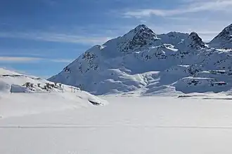 Sassal Mason über dem gefrorenen Lago Bianco und der Berninabahnlinie links