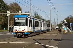 Amsterdam: Eine Sneltram verlässt die Station Sportlaan und überquert einen Bahnübergang (November 2014)
