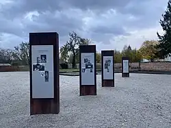 Auf hellem Untergrund sind die Stelen mit Biografien der Ermordeten zu sehen. Sie bestehen aus Metall, dass braun verrostet ist.