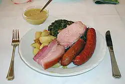 Typisches Grünkohlgericht mit Bratkartoffeln, Pinkel (mittig) sowie Kochwurst, Kassler und Speck, dazu Senf