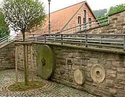 Mühlsteine der Graumühle, im Hintergrund das Wasserkraftwerk am früheren Mühlenstandort