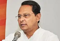 Hasanul Haq Inu. 2015. Bengalischer Mann mit Scheitel und Brille in einem weißen Hemd an einem Mikrofon.