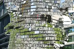 Ein Foto spiegelnder Bänder, die übereinander gelagert sind vor einer Hausfassade. Es lässt sich keine konkrete Form erkennen