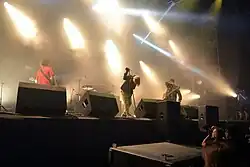 Die Bandmitglieder vom Bühnengraben Aus fotografiert. Von links nach rechts: Bassist Gary Mader steht am linken Bildrand mit dem Rücken zum Publikum. Vom Schlagzeuger Aaron Hill ist lediglich ein Stück des Kopfes sichtbar, der Rest des am Schlagzeug sitzenden Musikers ist von einer Monitorbox verdeckt. Mike Williams hält sich am Mikrofonständer fest und hat den Kopf gesenkt. Jimmy Bower steht mit der umgeschnallten Gitarre zu seinen Mitmusikern gewandt, den Arm vor die untere Gesichtshälfte haltend. Marder und Hill spielten während der Tournee ein Unbekanntes und unveröffentlichtes Stück, dass ausschließlich aus E-Bass und Schlagzeug bestand. Dabei fixierten beide einander.