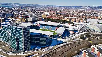 Das Stadiongelände von oben. Im Vordergrund das verglaste Hochhausgebäude Helsfyr Atrium. Am rechten Bildrand ist die Vallhall Arena zu sehen. (März 2018)
