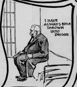 Ein älterer Most im gestreiften, schicken Anzug sitzt in einer Gefängniszelle.