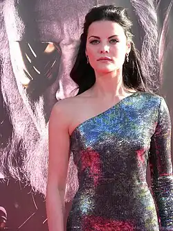 Jaimie Alexander mit ernstem Gesichtsausdruck bei der Weltpremiere des Films Thor 2011. Sie trägt ein auffälliges, schulterfreies Kleid, das in schimmernden Farben wie Blau, Rot und Grün gestaltet ist. Das Kleid hebt sich durch seine leuchtenden Farben und den eleganten Schnitt hervor. Im Hintergrund ist ein großes Poster des Films zu sehen, das einen Charakter mit einer Maske und einem langen Bart zeigt.