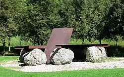 eine rostige Stahlplatte liegt auf großen Felsen, daraus ragt eine weitere rostige Stahlplatte schräg nach oben