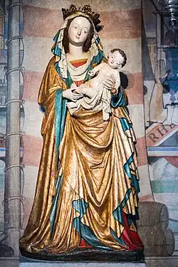 farbig gefasste Madonnenfigur mit weich fallendem Gewand. Hintergrund moderne Wandbemalung