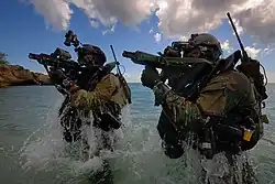 Zwei Kampfschwimmer kommen mit der Waffe im Anschlag kampfbereit aus dem Wasser.