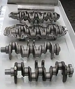 Zum Vergleich konventionell geschmiedete Kurbelwelle. Die hinteren beiden nach dem Schmieden, dann nach dem Abgraten, vorne nach dem Schleifen