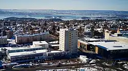 Foto von städtischer Bebauung. Im Hintergrund ist ein größeres Gewässer zu sehen, im Zentrum des Bildes befindet sich ein mehrstöckiger Wohnblock.