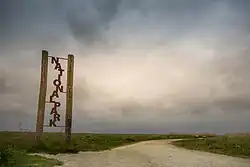 Über einer Grasfläche mit Sandweg ballen sich drohende Wolken. Am linken Bildrand ist ein Schild mit der Aufschrift „Nationalpark“.