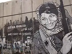Graffito. Zu sehen ist Leila Chaled mit um den Kopf geschlungener Kufiya, daneben der Schriftzug: „Leila Khaled. Don't forget the struggle“