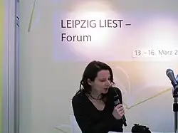 Martina Weber spricht in ein Mikrofon, über ihr ein Schriftzug "LEIPZIG LIEST - Forum"