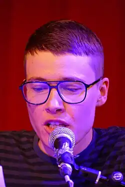 Eine junge Frau mit kurzen Haaren und Brille spricht in ein Mikrofon