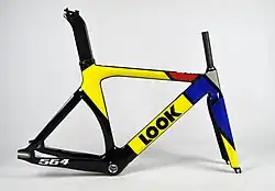 Ein Rahmen eines Bahnfahrrads steht vor einem weißen Hintergrund. Der Rahmen ist schwarz, worauf in gelb, rot, blaut und grau grobe geometrische Muster gemalt sind.