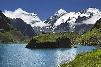 Grand Combin (links in Wolken), Combin de Corbassière (Mitte) und Petit Combin (ganz rechts) vom Lac de Louvie