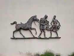 Das Bild zeigt das Bronzerelief mit St. Martin, der vom Pferd abgestiegen ist und einem Bettler die Hälfte seines Mantels gibt.