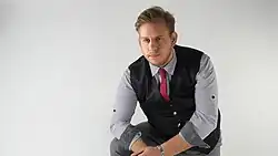 Marco Graf 2021, sitzend in vorgebeugter Haltung, trägt Hemd, Schlips und Weste