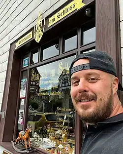 win Mann mit Bart und Kappe steht vor einem Ladengeschäft