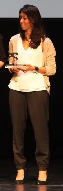 Matilde Ortiz trägt eine dunkle Hose, eine weiße Bluse und eine beige Jacke. In den Händen befindet sich eine Statue, die sie als Preis erhalten hat.