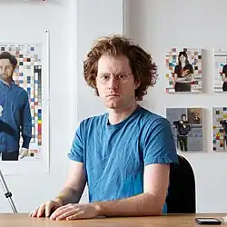 Porträt einer Person am Schreibtisch, blaues Shirt, Brille