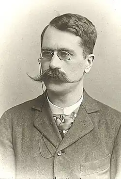 Michael Radaković mit Klemmbrille, Schnurrbart, Krawatte und in dunklem Anzug