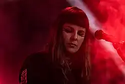 In einer Großaufnahme von Hélène de Thoury ist die Musikerin mit geschlossenen Augen hinter einem Mikrofon zu sehen.