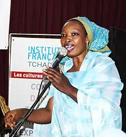 39-jährige Frau, in einem hellblauen Kleid mit einem blau-weißen Kopftuch singt in ein Mikrophon