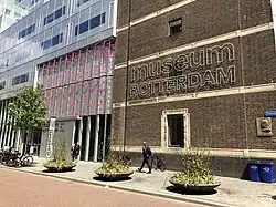 Eingang zum Museum Rotterdam von der Straßenseite. Der linke Gebäudeteil mit dem Eingang ist eine Stahl-Glas-Konstruktion, der rechte Teil ein Backsteinbau mit dem Namensschriftzug des Museums