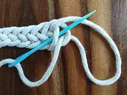 Schritt 2: /UOO = Nadel drehen, 1× unter einem Schlingenbogen hindurch, 2× über einen Schlingenbogen hinweg (anschließend Nadel durchziehen)