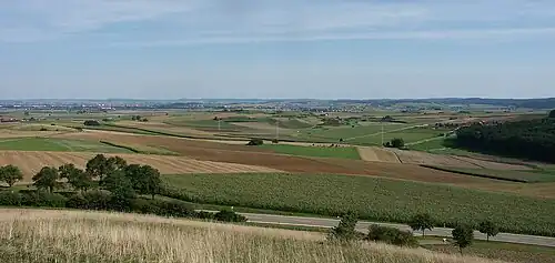 Blick ins Nördlinger Ries vom Blasenberg bei Kirchheim am Ries, links in der Ferne Nördlingen. Die bewaldeten Hügel am rechten Bildrand bilden den südlichen Kraterrand.