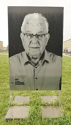 Zu sehen ist eine schwarz-weiß Fotografie die auf einer Wiese in Weimar in einer Metallkonstruktion steht. Naftali Fürst trägt kurzes helles Haar und trägt eine Brille.