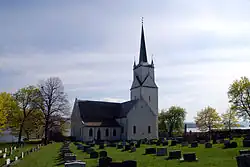 Foto einer Kirche, dahinter ein See, davor ein Friedhof