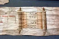 Torawimpel für Nathan bar Chajjim von 1888, mit Abbildung einer Torarolle und der Inschrift: „Eine Weisung hat uns Mosche geboten“ (vgl. Dtn 33,4 EU)