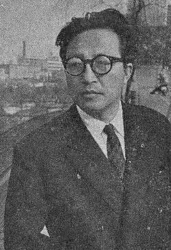 Bebrillter Mann mittleren Alters ab Brusthöhe in dunklem Jackett und weißem Hemd nebst dunkler Krawatte von vorn leicht nach links schauend in schwarzweiß.