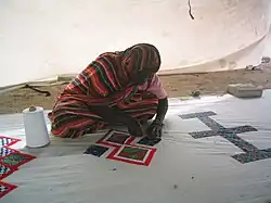 Eine verschleierte Frau sitzt auf einer großen Plane und näht Muster von Hand.