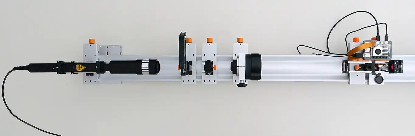 Optische Bank mit sechs Reitern und verschiedenen optomechatronischen Komponenten, wie Helium-Neon-Laser, Aufweitungsoptik, Linsen, Blende, Kollimatorobjektiv, Mikrolinsen-Array, Bildsensor und Mikrocomputer.