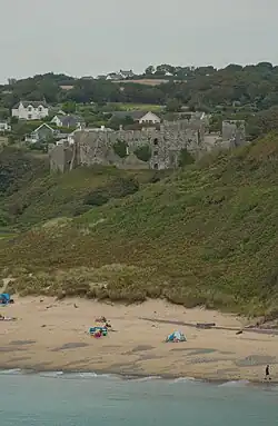 Eine Burgruine ragt über einen Sandstrand empor.