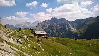 Das Rifugio Vallacia mit Blickrichtung Nordosten. Rechts der Bildmitte der Passo delle Selle mit der gleichnamigen Hütte. Links in der Ferne die Marmolata und der Gran Vernel.