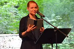 Cia Rinne an einem Lesepult stehend, ein geöffnetes Buch in der Hand