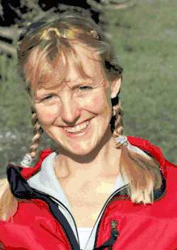 Daniela Jasper ist im Porträt frontal lächelnd in die Kamera schauend abgebildet. Sie hat blondes zu zwei Zöpfen geflochtenes Haar, welche auf Schulterhöhe enden. Sie trägt einen roten sportlich wirkenden Pullover mit Reißverschluss, der aufgezurrt ist. Im Hintergrund ist eine Wiese oder grüne Landschaft auszumachen.